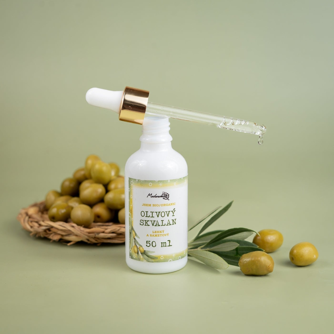 Organic olive squalane facial oil 50 ml in a white dropper bottle with pipette, surrounded by fresh green olives on a soft green background.